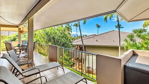 A balcony with lounge chairs, a railing, and a view of palm trees and a building. - Kaanapali Condo - 1BR/2BA - Beach Cabana, Pools, Private Lanai, A/C (Lahaina)