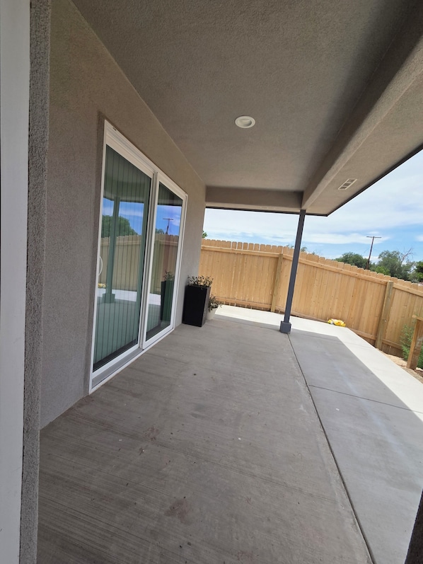 A covered patio area with a concrete floor, a wooden fence in the background, and a potted plant.