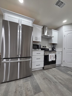 A kitchen with a stainless steel refrigerator, white cabinets, a microwave, an oven, and a tiled floor.