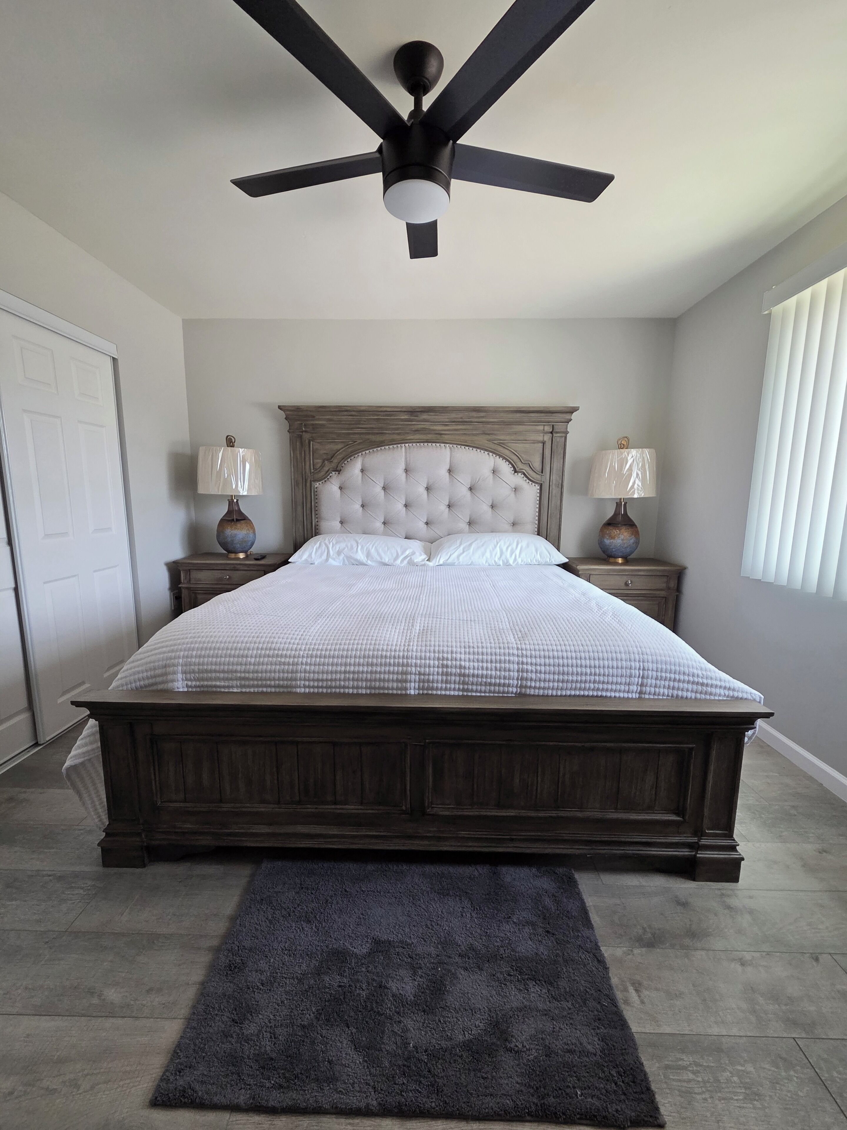 A bedroom with a large bed, a ceiling fan, two bedside lamps, and a dark rug.