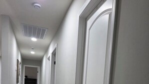 En hall med vita dörrar, en ventilationsöppning i taket och en lampa.
