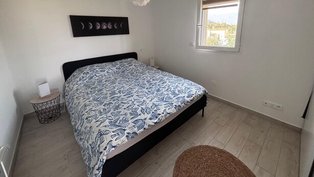 Un dormitorio con cama, una mesita de noche pequeña, una obra de arte en la pared, ventana con persianas y un ventilador de techo.