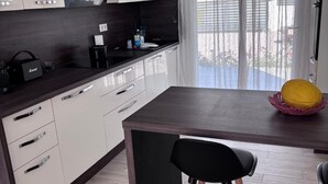Una cocina moderna con armarios blancos, encimera oscura y una ventana con cortinas translúcidas.