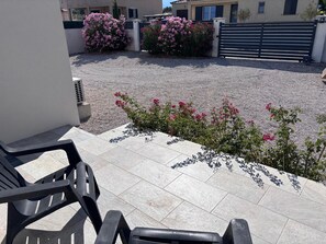 Ein Patio mit Kiesfläche, einem schwarzen Metallgitter und pinkfarbenen blühenden Pflanzen.