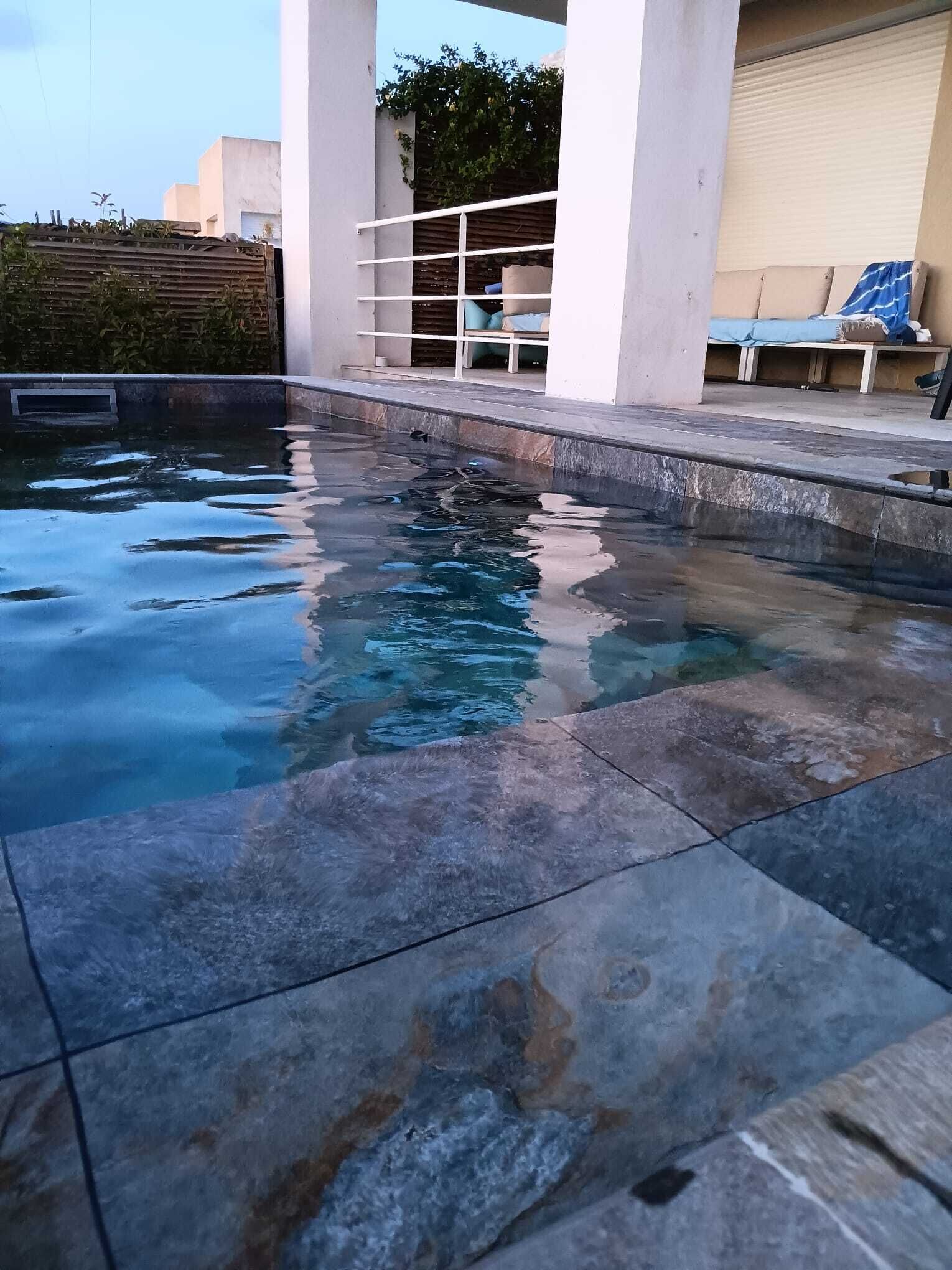 A swimming pool with clear water, surrounded by stone tiles.