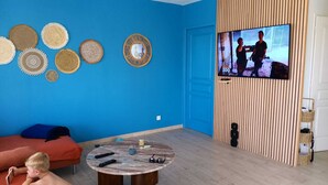 Una sala de estar con una pared azul, una mesa de centro redonda y un televisor mostrando un programa.