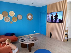 Ein Wohnzimmer mit blauer Wand, einem runden Couchtisch und einem Fernseher, der ein Programm zeigt.