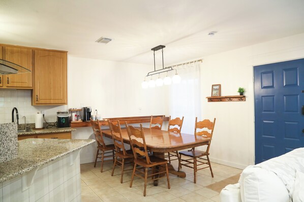 A kitchen with a dining table, chairs, a coffee maker, and a blue door. - Texan Cottage Getaway —Near UTSA, Six Flags, Seaworld; Family Recreation & Trail (San Antonio)