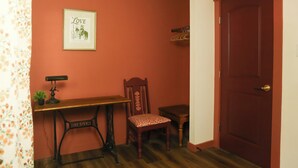 Una habitació amb una paret vermella, un escriptori de fusta, una cadira, una porta i un quadre encimbellat a la paret.