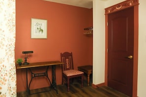 Una habitación con pared roja, un escritorio de madera, una silla, una puerta y un cuadro enmarcado en la pared.