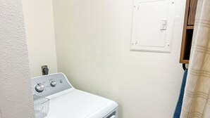 Une petite buanderie équipée d’un lave-linge blanc, d’une prise électrique murale et d’une porte dotée d’un interrupteur pour la lumière.