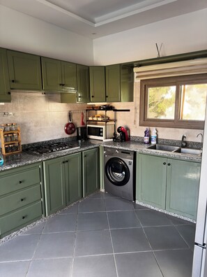 A compact kitchen with green cabinets, a built-in microwave, a washing machine, and a window above the sink. - Villa Sylvester, Essaouira (Essaouira)