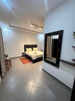 A modern bedroom with a large bed, a nightstand, a mirror, and a red rug. - Villa Sylvester, Essaouira (Essaouira)