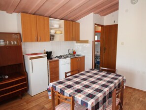 A compact kitchen with wooden cabinets, a white refrigerator, a gas stove, and a table with a checkered tablecloth. - Boho Apartment Oma Maria / HR-11059-03 by Interhome (Dracevac)