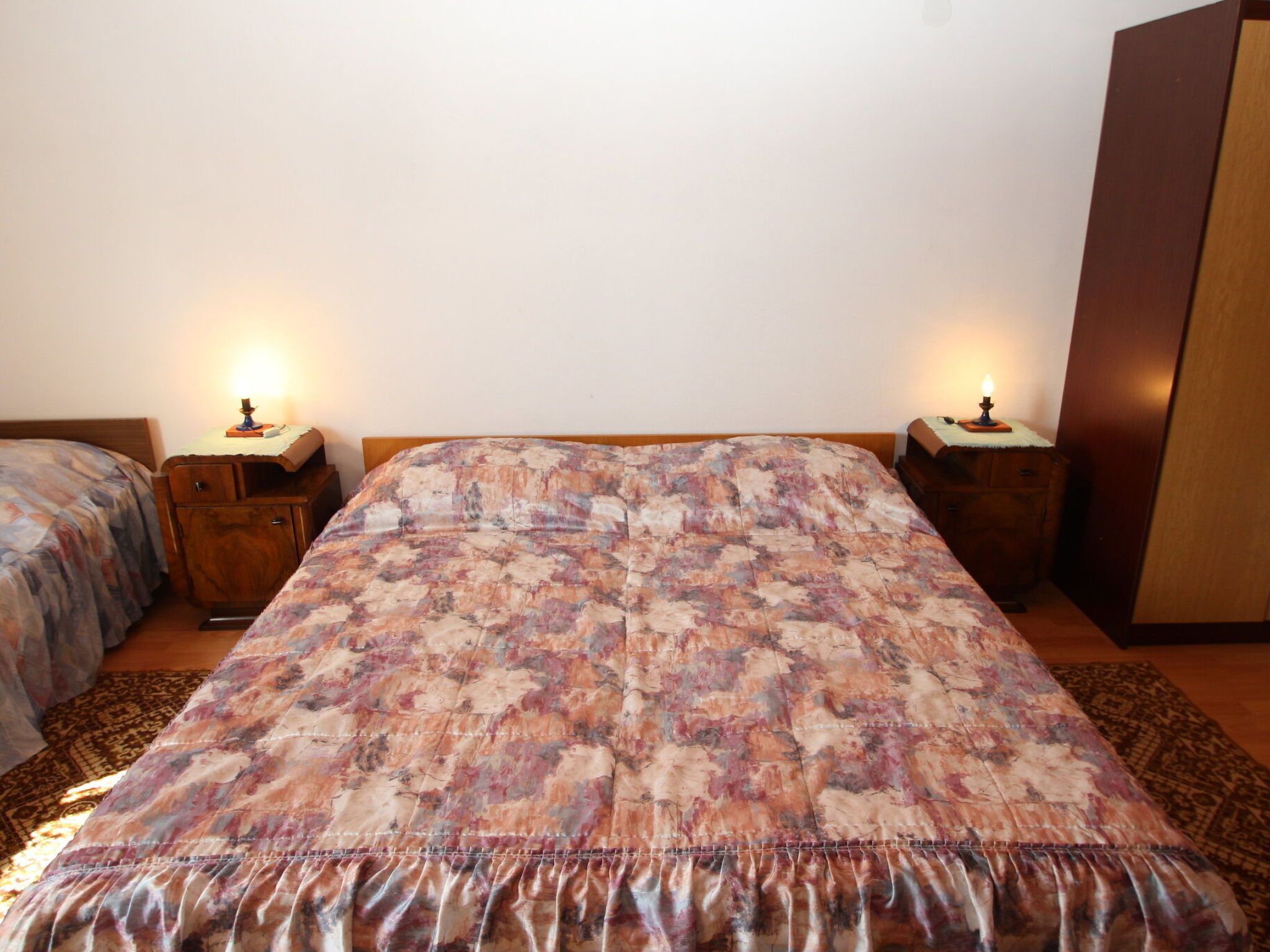 A bedroom with a large bed, two bedside tables with lamps, and a wardrobe.
