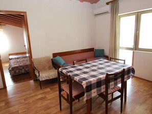 A room with a wooden floor, a table with a checkered tablecloth, a sofa with cushions, a bed with a patterned blanket, and a window with curtains. - Boho Apartment Oma Maria / HR-11059-03 by Interhome (Dracevac)