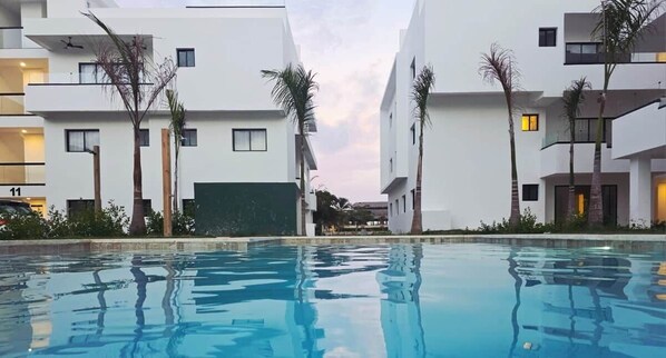 Un hôtel moderne doté d’une piscine, d’une façade blanche et de palmiers.