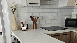 A modern kitchen with a white countertop, wooden cabinets, and a black stove. There are two black bar stools and a vase with flowers on the counter. - Apartment for Airbnb Punta Cana - ONA Resident 2BR (Punta Cana)