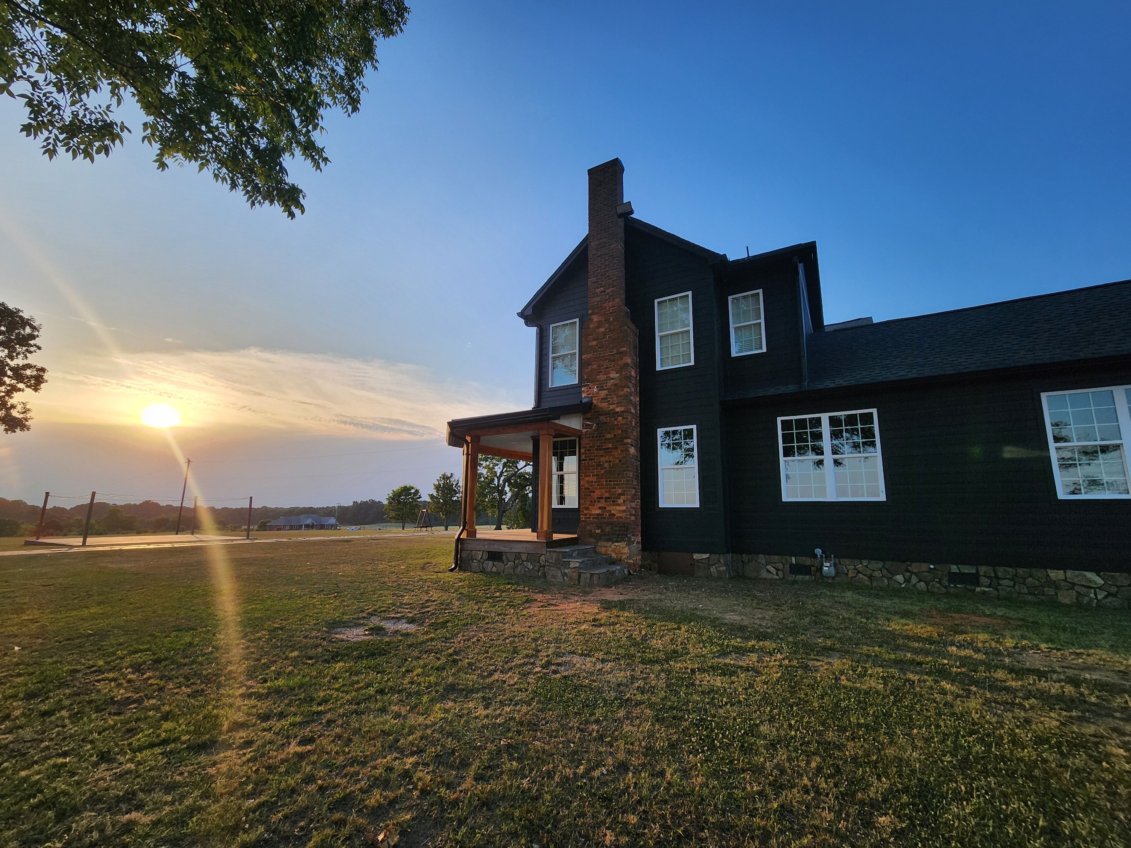 A two-story house with a stone chimney, a covered porch, and a grassy yard.