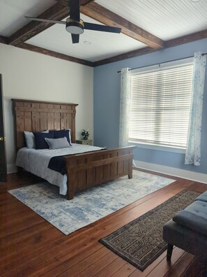 A bedroom with a wooden bed, a ceiling fan, a window with blinds, and a patterned rug.