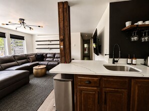 A modern kitchen with a central island, wooden cabinets, and a built-in TV. - Base Camp Breckenridge | Aspens · Hot Tub · Dogs (Breckenridge)