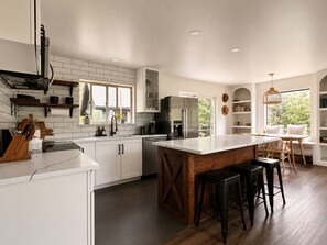 A modern kitchen with white cabinetry, a large island, and a dining area with a view. - Base Camp Breckenridge | Aspens · Hot Tub · Dogs (Breckenridge)