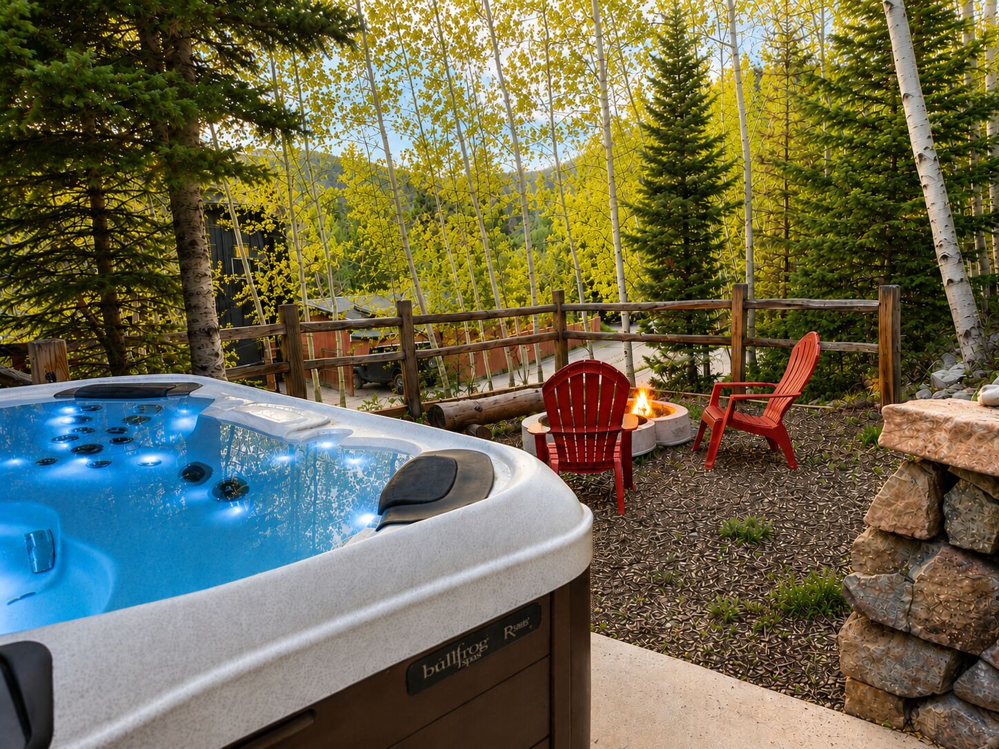 A hot tub with a wooden deck, two red Adirondack chairs, and a stone wall.