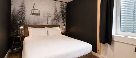 Une chambre à coucher comprenant un lit, une table de chevet, une lampe fixée au mur, une fenêtre avec des rideaux et une fresque murale.