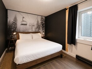 Ein Schlafzimmer mit einem Bett, einem Nachttisch, einer Wandlampe, einem Fenster mit Vorhängen und einem Wandbild.