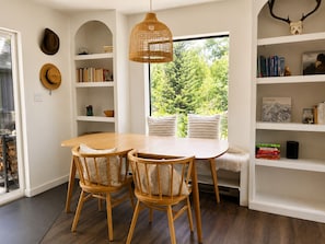 Ein Essbereich mit einem runden Tisch und Stühlen, ein Bücherregal mit Büchern und Dekoration sowie ein Fenster mit Blick ins Grüne.