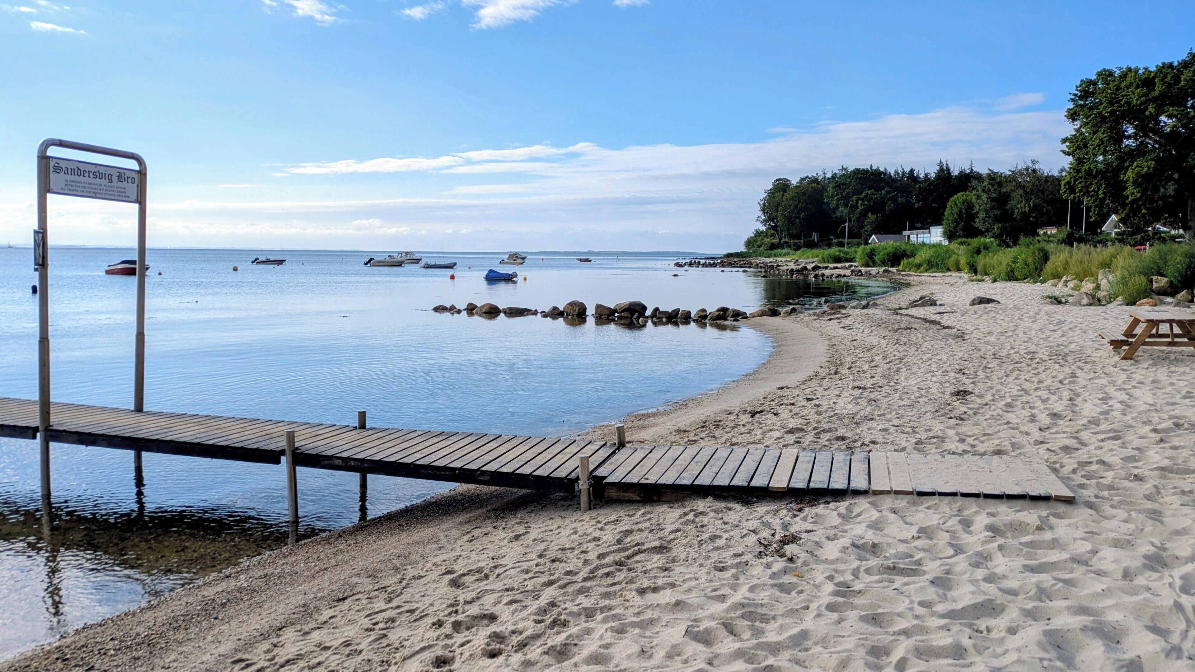 A sandy beach with a wooden pier and a sign.