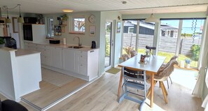 A modern kitchen with white cabinets, a dining area with a table and chairs, and large windows offering a view of the outdoors. - Cozy holiday home near the beach (Haderslev)