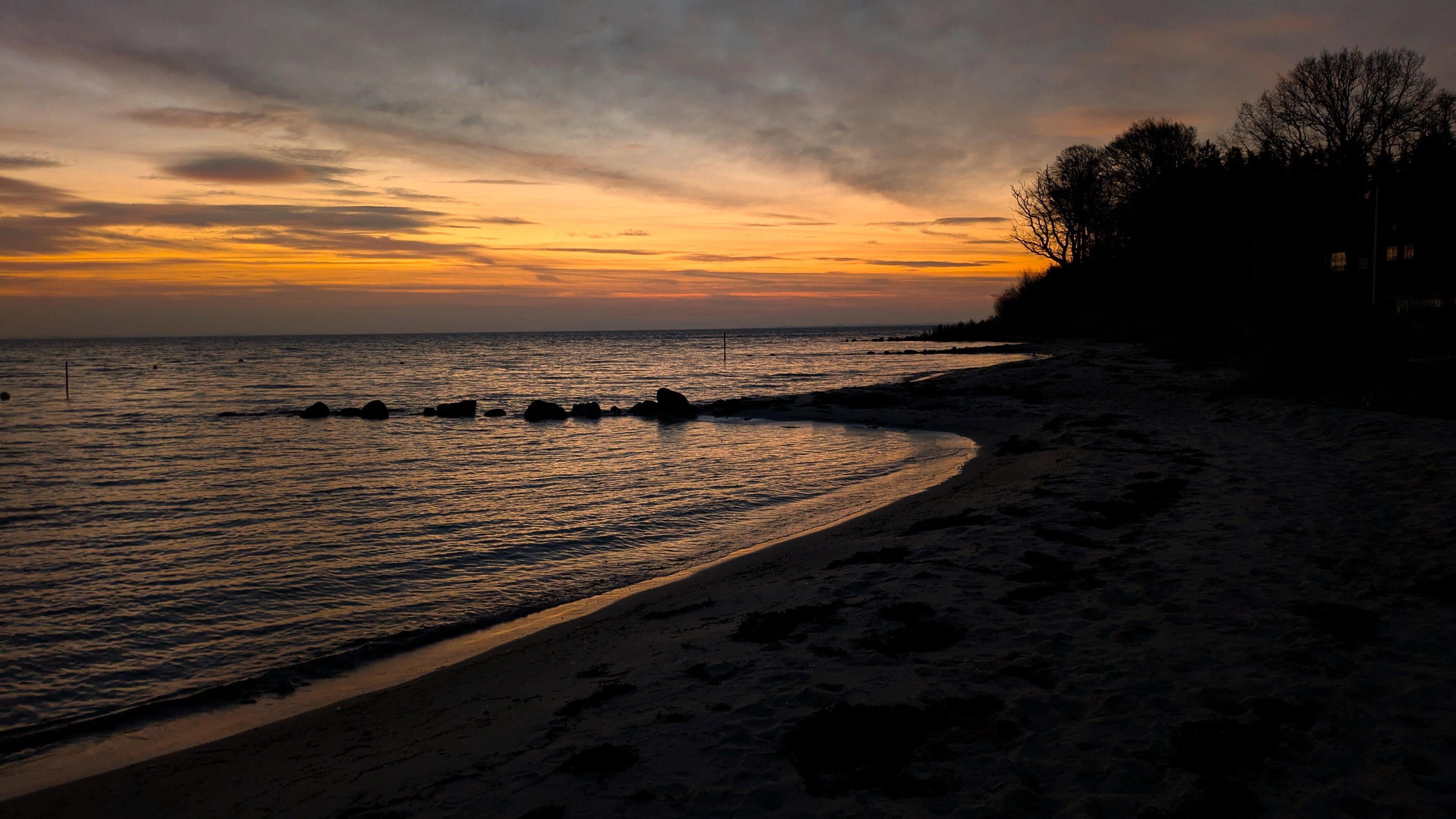 A beach with a curved shoreline, calm water, and a sunset sky.