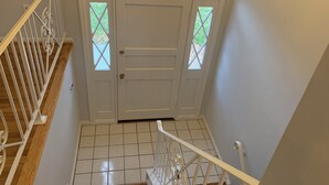 Eine weiße Tür mit Fenster, eine Holztreppe mit weißen Geländern und ein Fliesenboden.