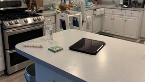 Eine moderne Küche mit weißen Schränken, Edelstahlgeräten und einer Arbeitsplatte mit einem Tablet und einer Wasserflasche.