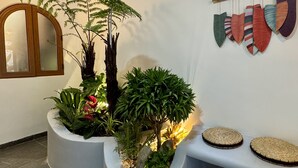 En reception med plantearrangement, et spejl og en dekorativ genstand på væggen.