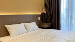 Et hotelværelse med seng, natbord, spejl og et vindue med gardiner.