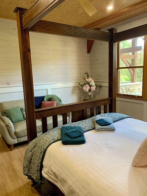 Ein Schlafzimmer mit einem hölzernen Himmelbett, einer Couch mit Kissen, einer Vase mit Blumen und einem Fenster mit Blick.