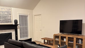 A living room with a black leather sofa, a wooden coffee table, a flat-screen TV, a fireplace, and a bookshelf. - Spacious 3BR House in Frisco - Minutes from Top Event Attractions (Frisco)