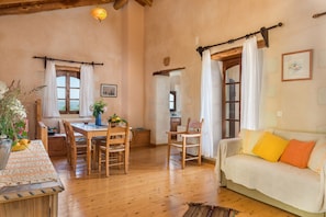 A rustic interior with a dining area, a sofa, and a view through an open doorway. - Kamares Private Pool stone Villa (Macheri)