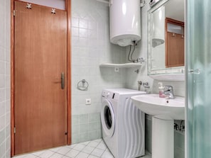 Ein Badezimmer mit Holztür, einer Waschmaschine, einem Waschbecken und einem Spiegel.