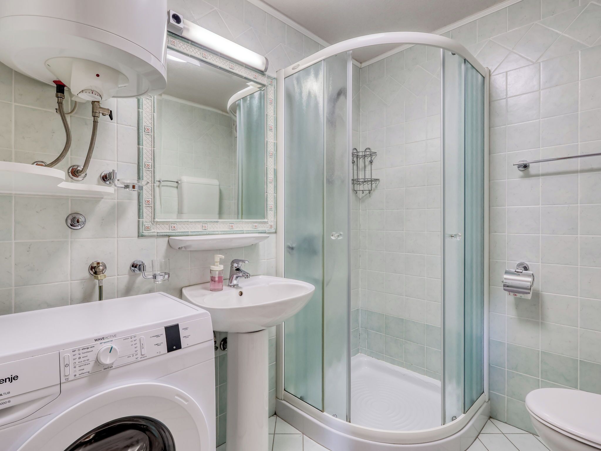 A modern bathroom with a washing machine, sink, glass shower enclosure, and toilet.