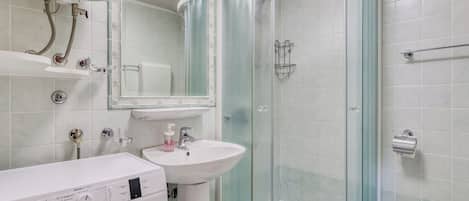 A modern bathroom with a washing machine, sink, glass shower enclosure, and toilet.
