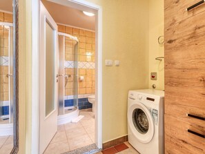 Ein Badezimmer mit Duschkabine aus Glas, einer Waschmaschine und einem Holzschrank.