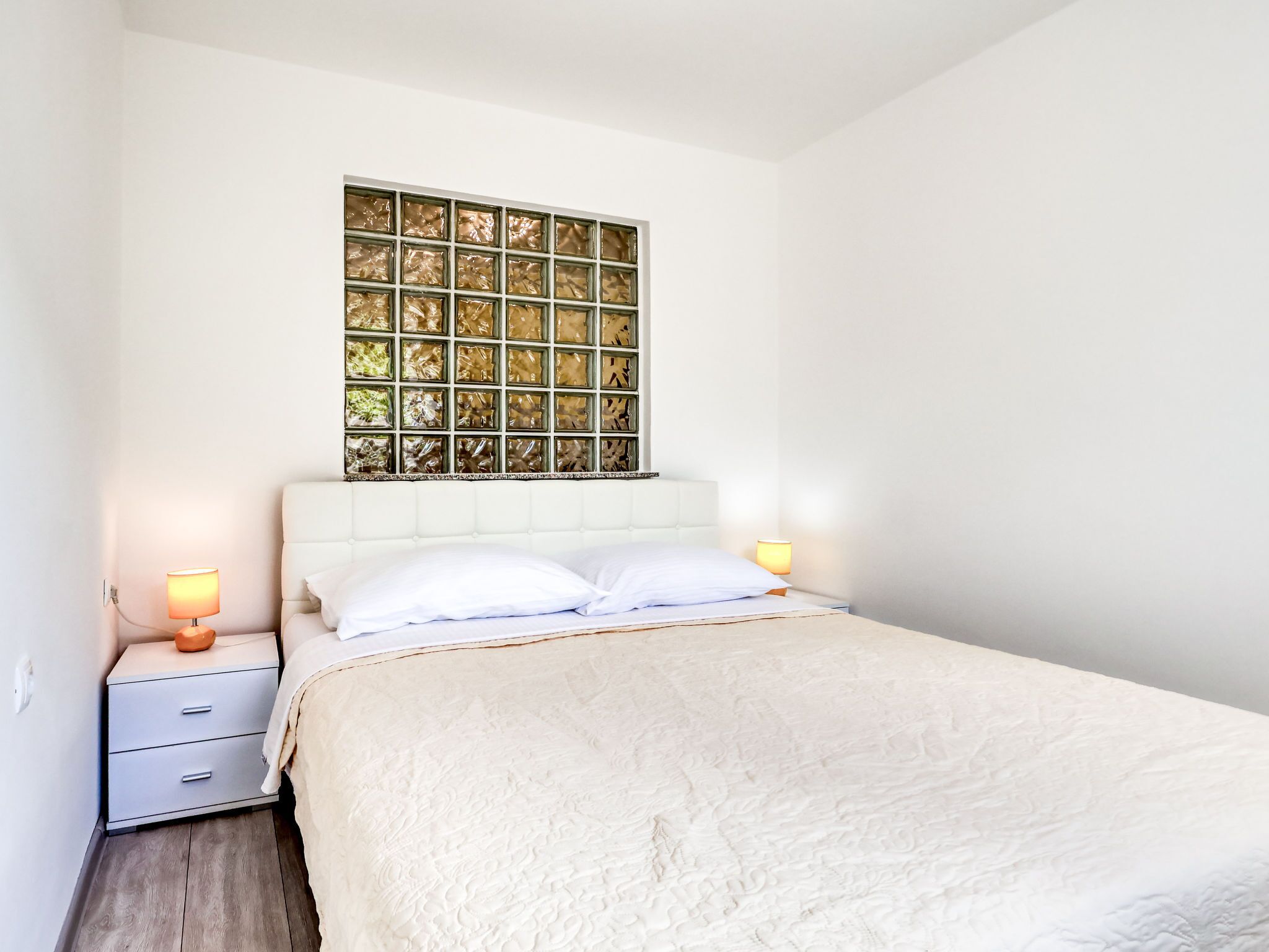 A bedroom with a bed, two bedside lamps, a nightstand, and a decorative window with a grid pattern.