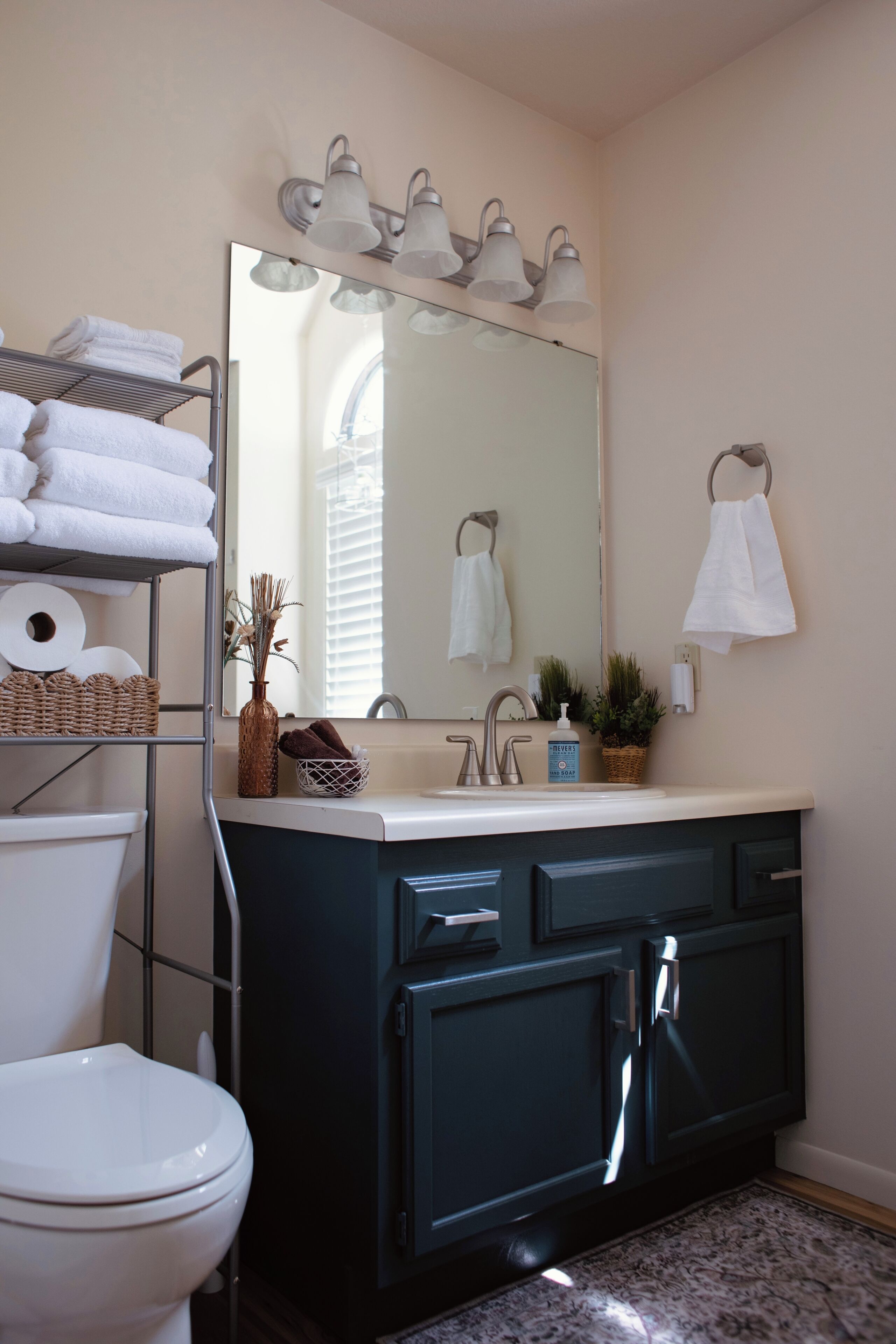 A bathroom with a white toilet, a dark blue vanity with a mirror above, and a towel rack on the wall.