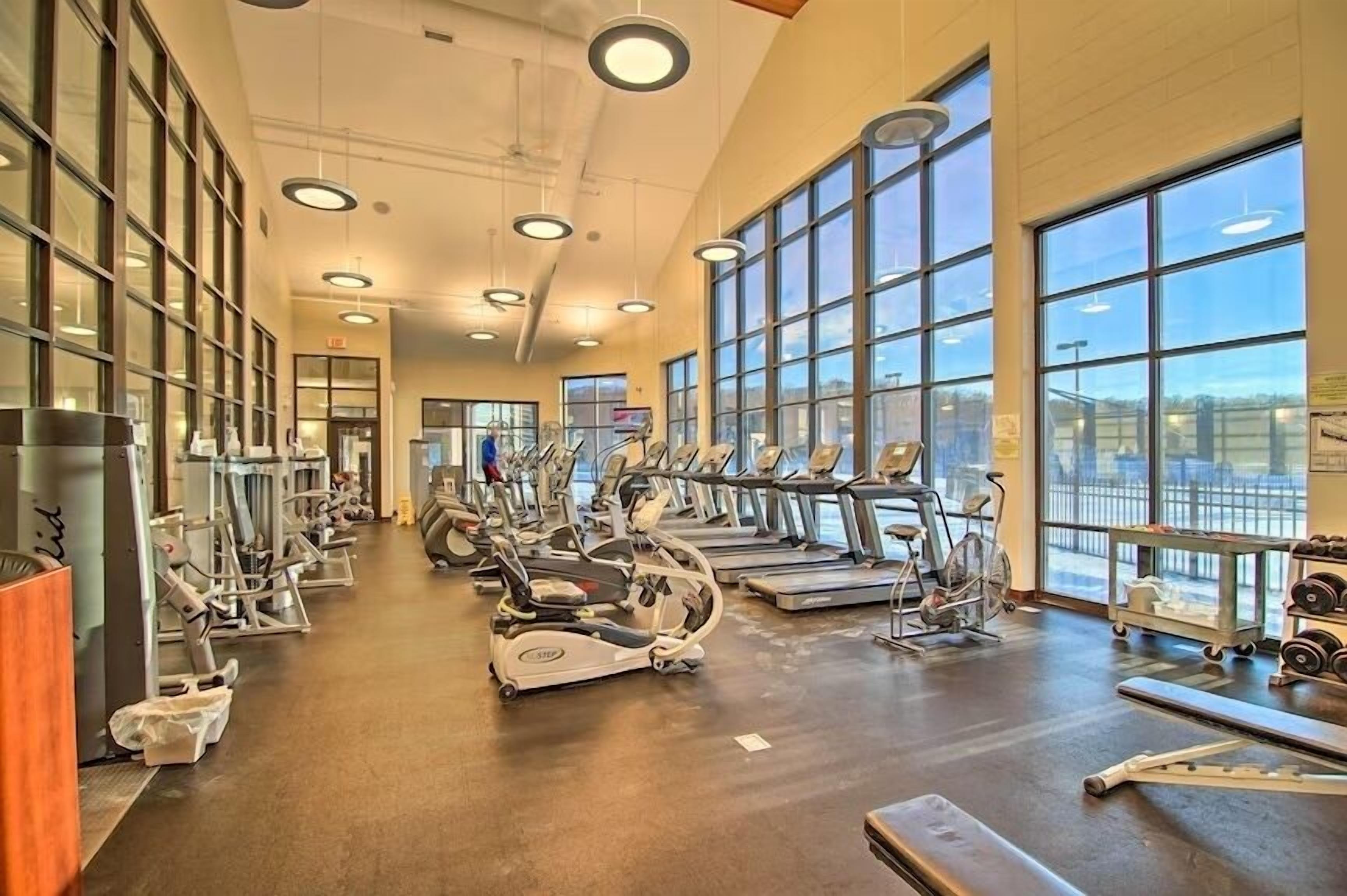 Un gimnasio con máquinas de cardio, equipo de levantamiento de pesas y grandes ventanales.