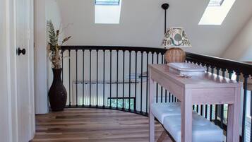 Een kamer met een houten vloer, een witte deur, een zwarte leuning en een klein raam.