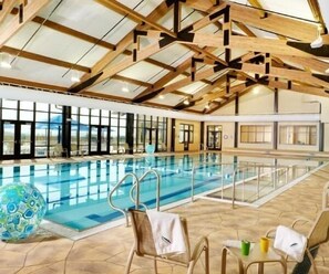 An indoor swimming pool with a wooden ceiling and large windows.