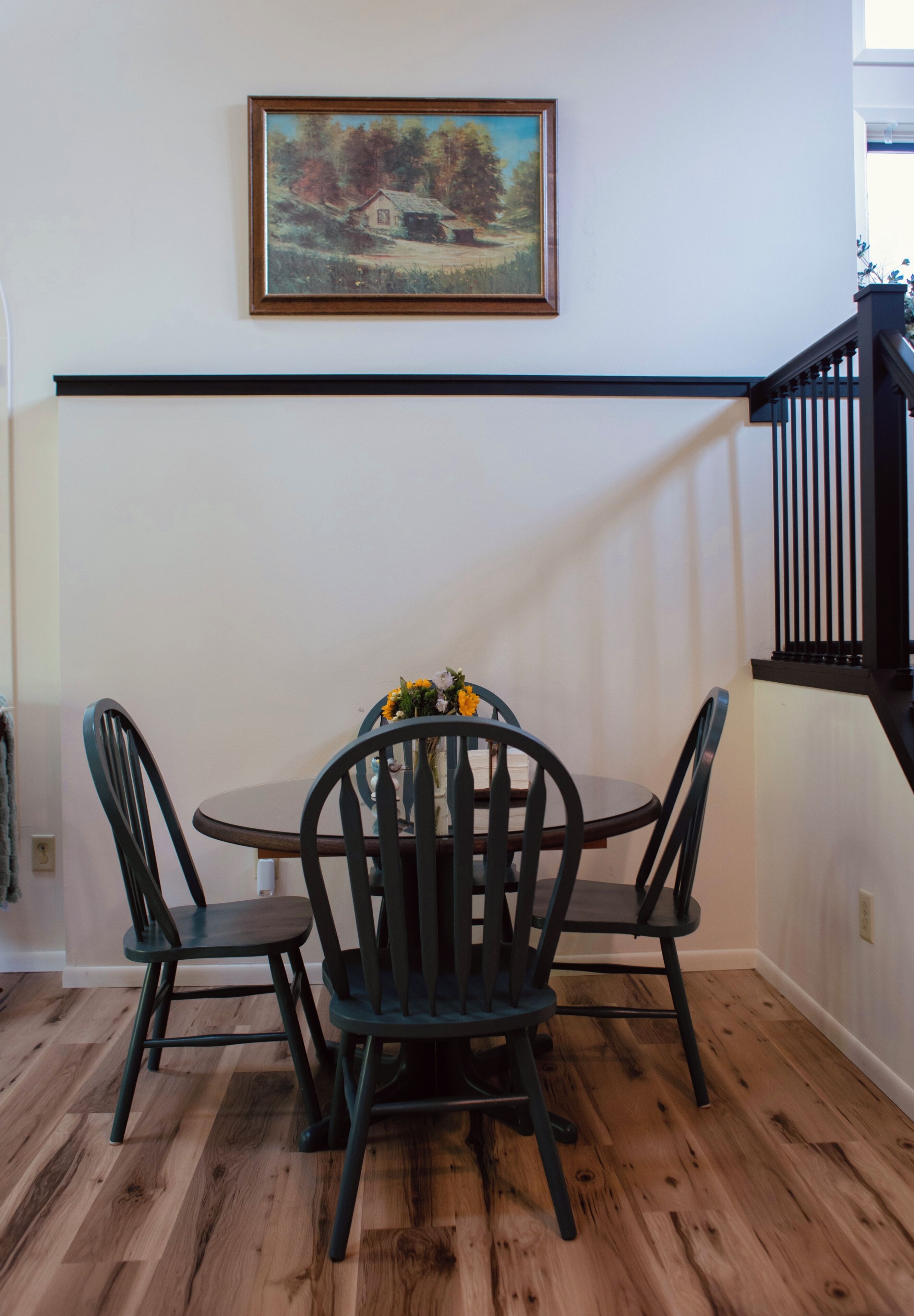 Un coin repas avec une table et des chaises, un tableau accroché au mur et un escalier.
